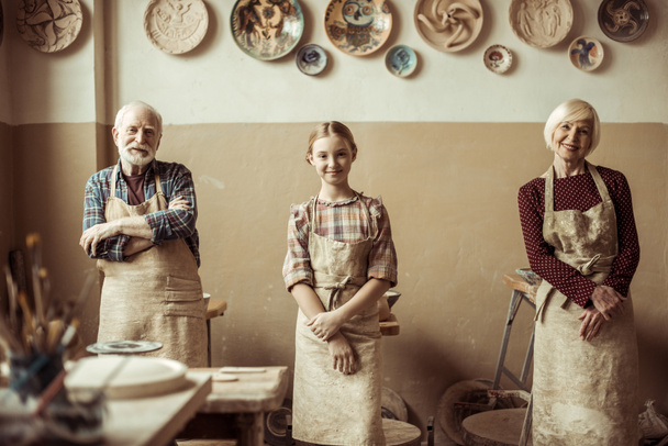 Бабушка и дедушка с внучкой стоят в ряд в мастерской
 - Фото, изображение