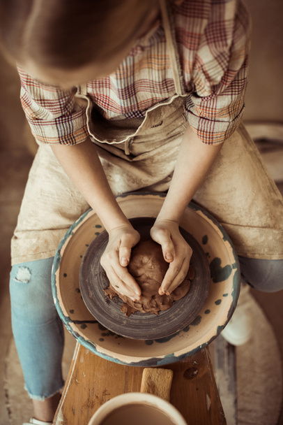 Вид сверху на маленькую девочку, делающую керамику на колесах в мастерской
 - Фото, изображение