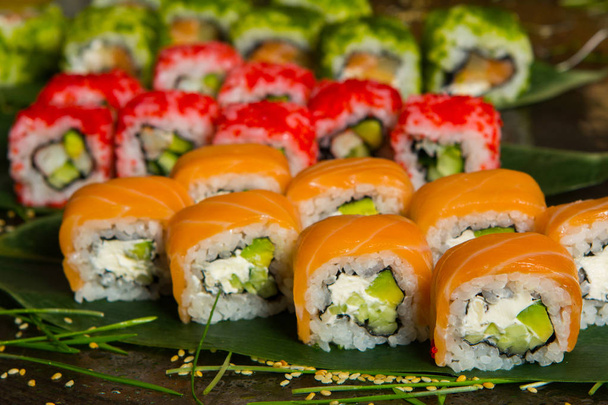 Różnego rodzaju jedzenie sushi serwowane na czarnym tle. Zbliżenie na smaczny świeże sushi rolls z ryb i ryżu na talerzu. Sushi rolki serwowane na drewnianej tablicy w restauracji - Zdjęcie, obraz