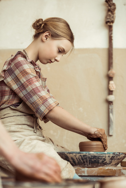 Vista lateral de la niña haciendo cerámica en la rueda en el taller
 - Foto, Imagen