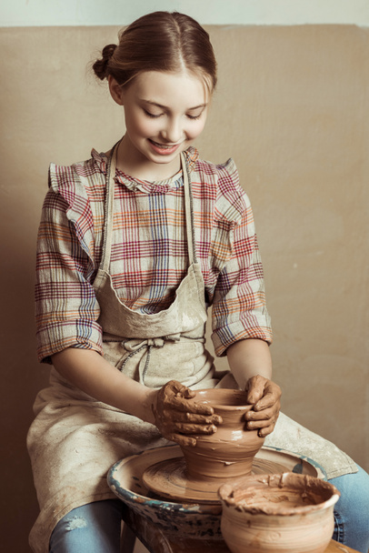 Front view of little girl making pottery on wheel at workshop - Photo, Image