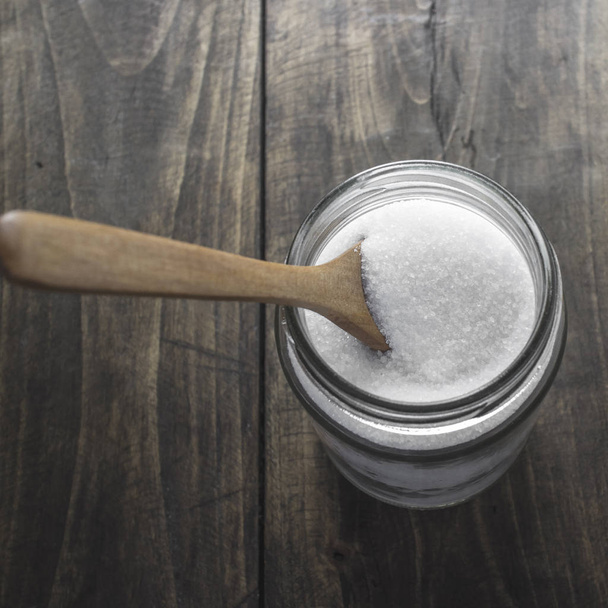 Sugar in wooden spoon and glass jar - Фото, изображение