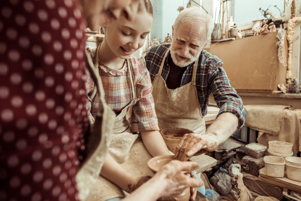 Avó e avô com neta fazendo cerâmica na oficina
 - Foto, Imagem