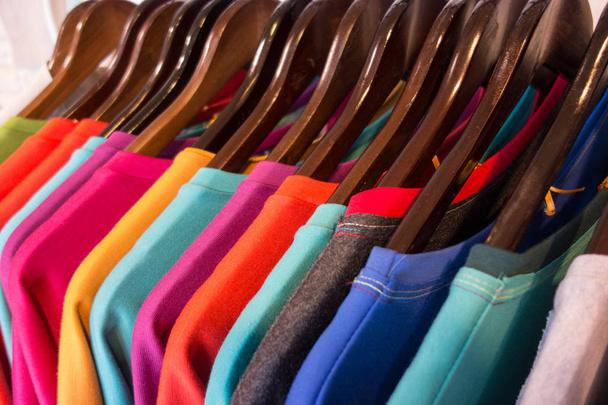 Лінія різнокольорового одягу на дерев'яних вішалках в магазині. Продаж
 - Фото, зображення