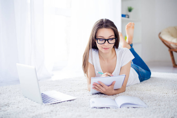 Happy young successful girl is making notes at home lying on the - Foto, afbeelding