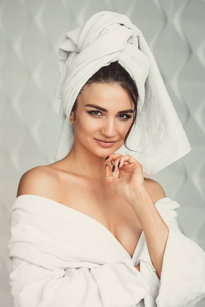 sexy young girl with dark hair, big eyes and dark eyebrows wearing white bath robe whith towel on her head. - Фото, изображение
