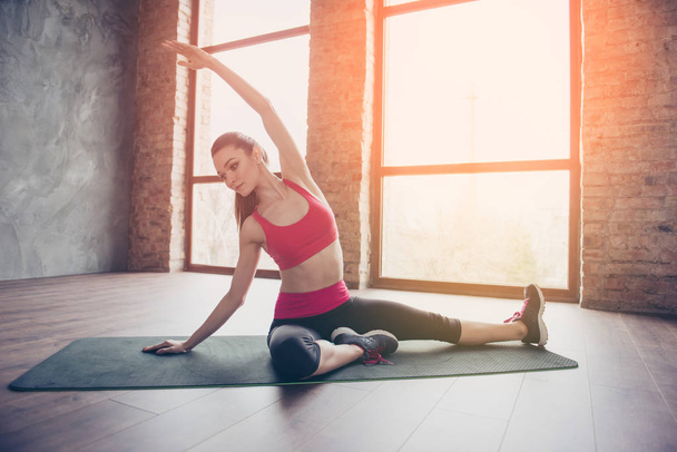 Young sportwoman is making stretching on green mat on the floor  - 写真・画像