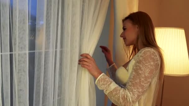 vrouw in wit nachtkleding kijkt uit een raam - Video
