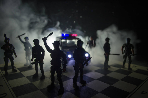 Полиция по борьбе с беспорядками подает сигнал быть готовой. Концепция государственной власти. Полиция на шахматной доске. Дым на темном фоне с огнями. Сиреневые сирены
 - Фото, изображение