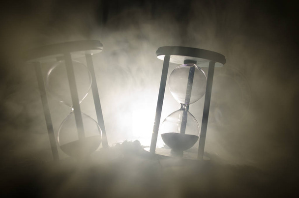 Концепция времени Силуэт часов Песочные часы и дым на темном фоне с горячим желтым оранжевым освещением, или символы времени с копировальным пространством, песочные часы или песочные часы
 - Фото, изображение