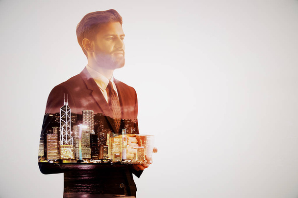 Handsome thoughtful young businessman drinking coffee on abstract night city background. Employment concept. Double exposure - Фото, изображение