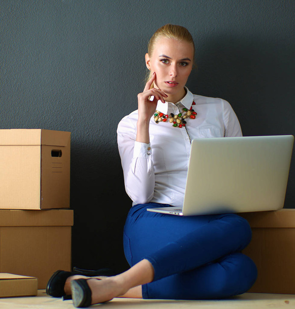 Woman sitting on the floor near a boxes  with laptop - Foto, imagen