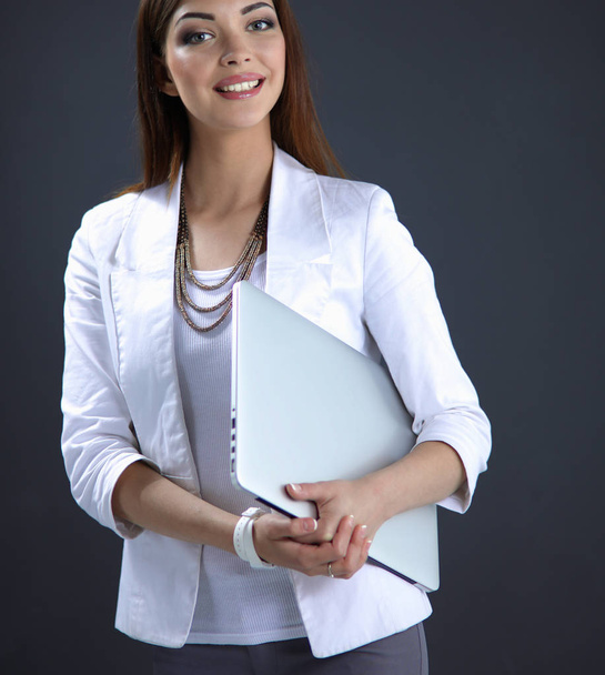 Young woman holding a laptop, standing on gray background - Foto, afbeelding