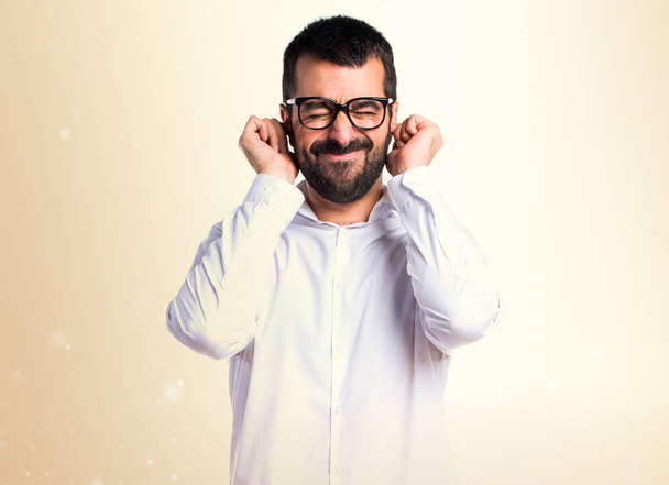 Όμορφος άνδρας με γυαλιά που καλύπτουν τα αυτιά του σε φόντο ώχρα - Φωτογραφία, εικόνα