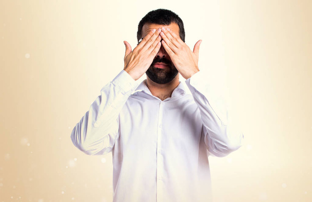 Komea silmälasipäinen mies peittää silmänsä okran taustalla
 - Valokuva, kuva