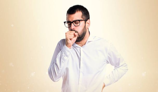 Handsome man with glasses coughing a lot on ocher background - Photo, Image