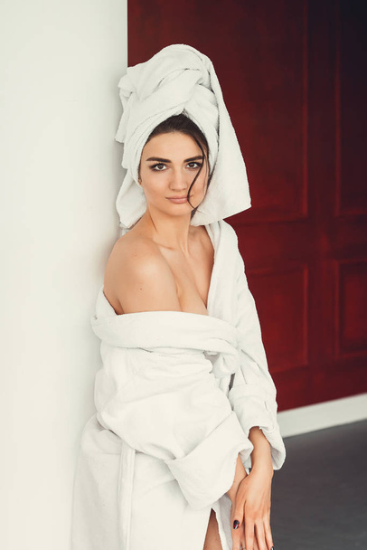 sexy young girl with dark hair, big eyes and dark eyebrows wearing white bath robe whith towel on her head. - Foto, Imagem