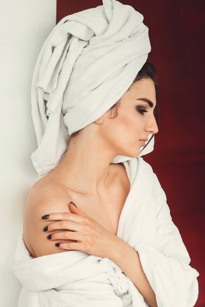 sexy young girl with dark hair, big eyes and dark eyebrows wearing white bath robe whith towel on her head. - Фото, изображение