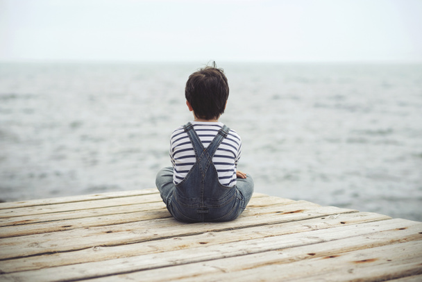 A criança pensativa senta-se à beira-mar. Visão traseira
 - Foto, Imagem