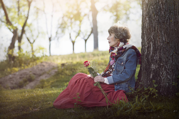 mujer mayor pensativa sentada en la hierba
 - Foto, imagen