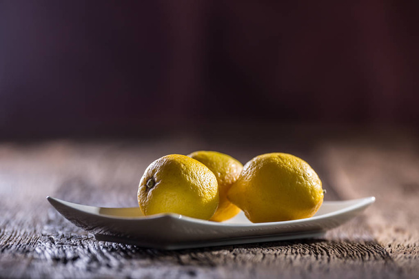 Лемон. Свежие лимоны в белой миске на столе
 - Фото, изображение