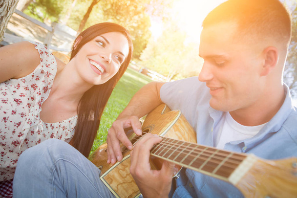 Счастливая смешанная расовая пара в парке играет на гитаре и поет S
 - Фото, изображение