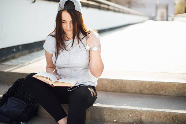 Pretty girl sit on the steps and read book with headphones - Foto, Imagem