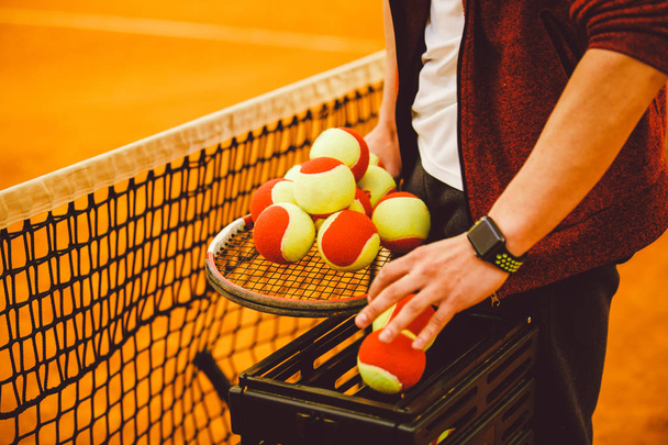 άνθρωπος χέρι που κρατά μια ρακέτα του τένις και πολλά γκολ. Καλάθι για μπάλες του τένις, - Φωτογραφία, εικόνα