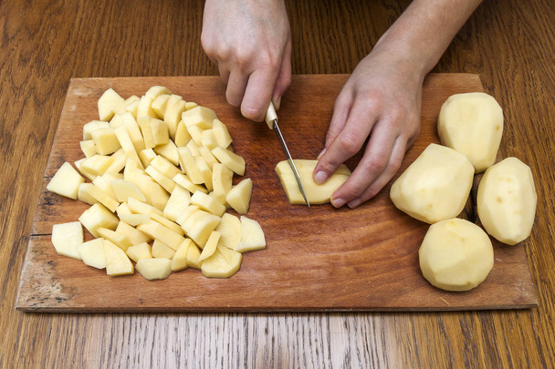 Woman's hand with a knife cutting slicing potatoes on wooden boa - 写真・画像