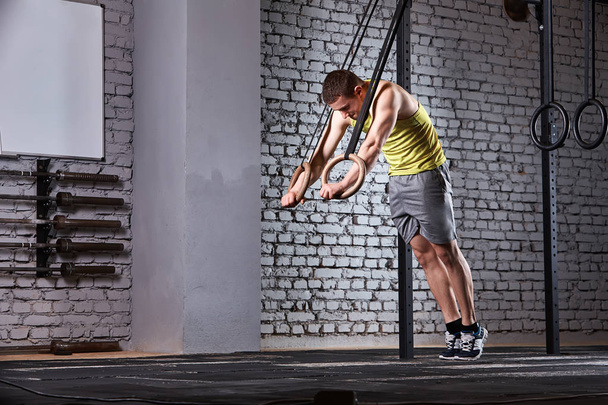 Young athletic man in the sportwear training at the cross fit gym with rings against brick wall. - Fotoğraf, Görsel