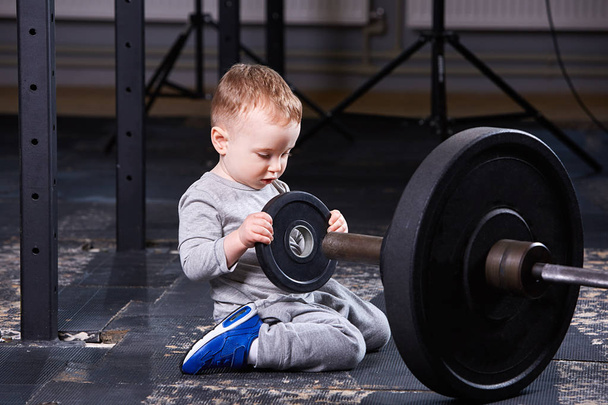Little cute child in sportwear in the cross fit gym with a barbell. - Фото, изображение
