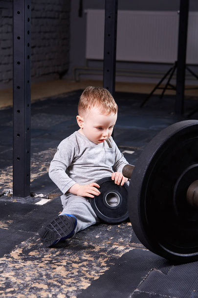 Little cute child in sportwear in the cross fit gym with a barbell. - Foto, Imagem