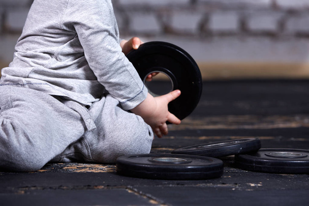 Close-up photo of little boy with barbell against brick wall in the cross fit gym. - Fotoğraf, Görsel