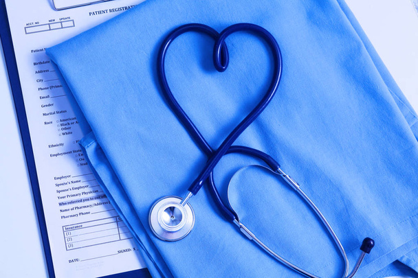 Estetoscopio médico retorcido en forma de corazón que se encuentra en la lista de antecedentes médicos del paciente y primer plano uniforme médico azul
 - Foto, imagen
