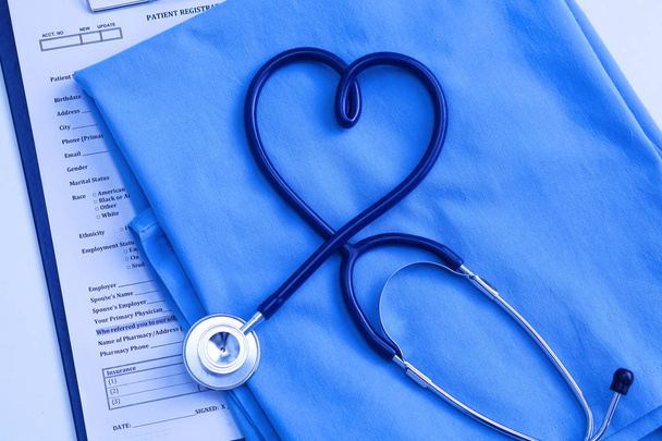 Stetoscopio medico attorcigliato a forma di cuore che giace sulla lista anamnesi del paziente e primo piano uniforme medico blu
 - Foto, immagini