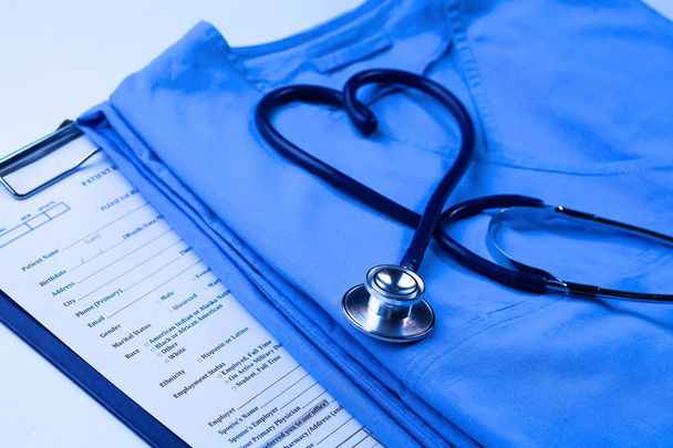 Estetoscopio médico retorcido en forma de corazón que se encuentra en la lista de antecedentes médicos del paciente y primer plano uniforme médico azul
 - Foto, Imagen