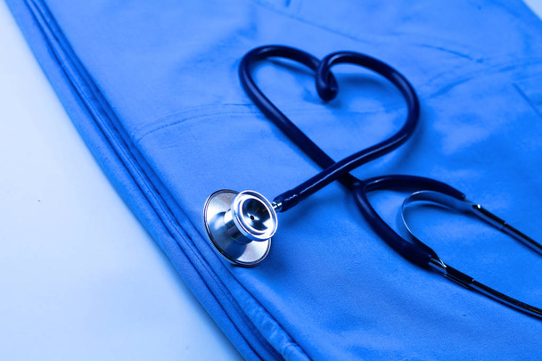 Медицинский стетоскоп скрученный в форме сердца, лежащий в списке пациентов и синей униформе врача крупным планом
 - Фото, изображение