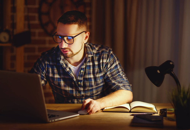 ο άνθρωπος που εργάζονται στον υπολογιστή στο σπίτι το βράδυ στο σκοτάδι  - Φωτογραφία, εικόνα