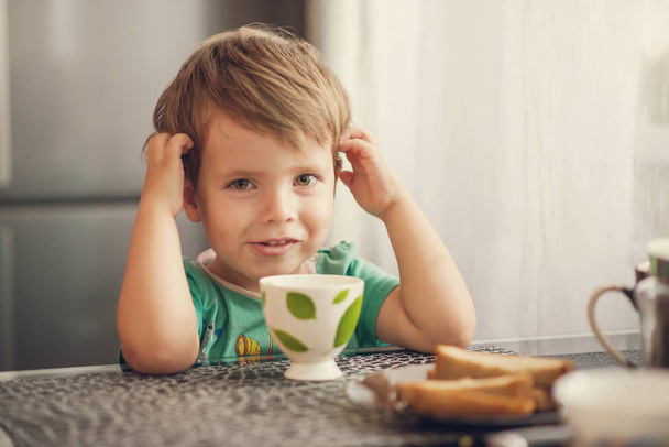 Cheerful boy drinks milk, eats toast for breakfast - Fotoğraf, Görsel