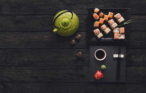 Set of sushi and rolls with teapot on black rustic wood, top view - Photo, Image