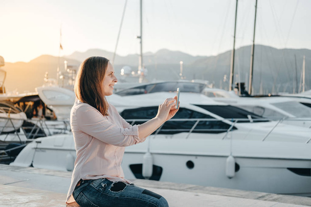 Young hipster woman taking photo  while sitting near sea port - Φωτογραφία, εικόνα
