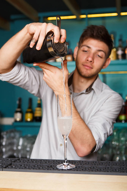 Νεαρός μπάρμαν όμορφος ρίχνει το ποτό σε ένα ποτήρι κοκτέιλ - Φωτογραφία, εικόνα