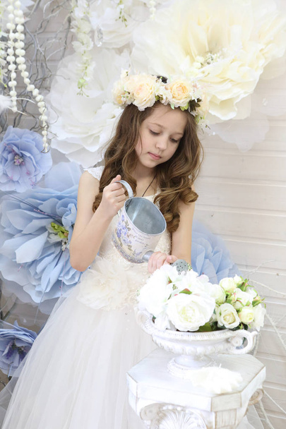 girl in a wreath and a white dress watering flowers - 写真・画像