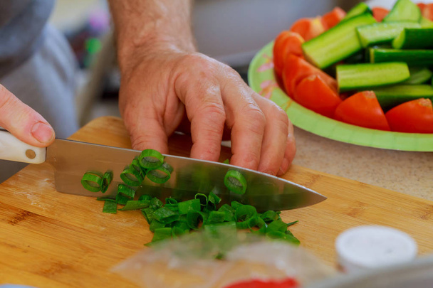 Couper l'oignon vert avec un couteau de cuisine sur une planche à découper en bois. Oignons verts frais sur une planche à découper
. - Photo, image