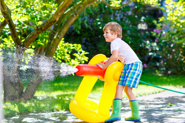 μικρό παιδί αγόρι παίζει με μια μάνικα κήπων ψεκαστήρων νερού - Φωτογραφία, εικόνα