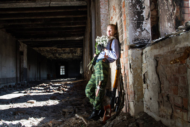 Girl sniper on the ruins with a bouquet of flowers - Photo, Image