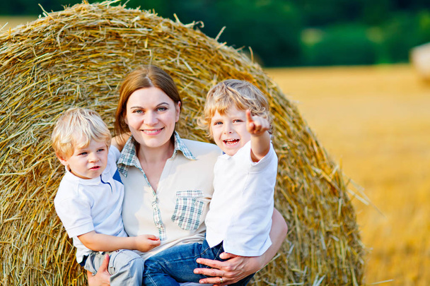 Äiti pitelee kahta lasta aseissa vehnäpellolla kesällä
 - Valokuva, kuva