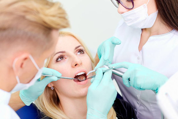 Two dentists treat their teeth to  visitor in dental office - Foto, imagen