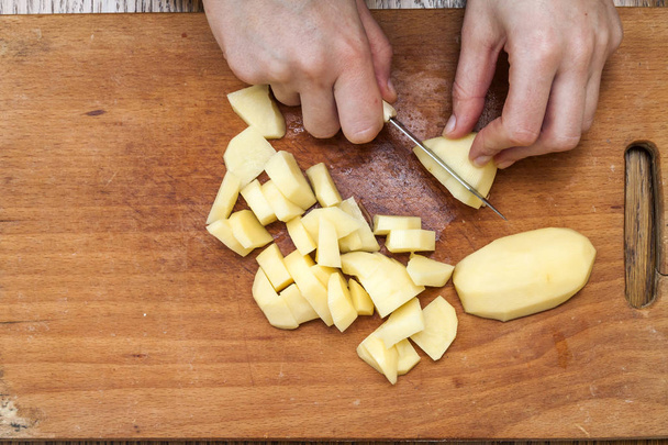 Main de femme avec un couteau tranchant des pommes de terre sur un boa en bois
 - Photo, image