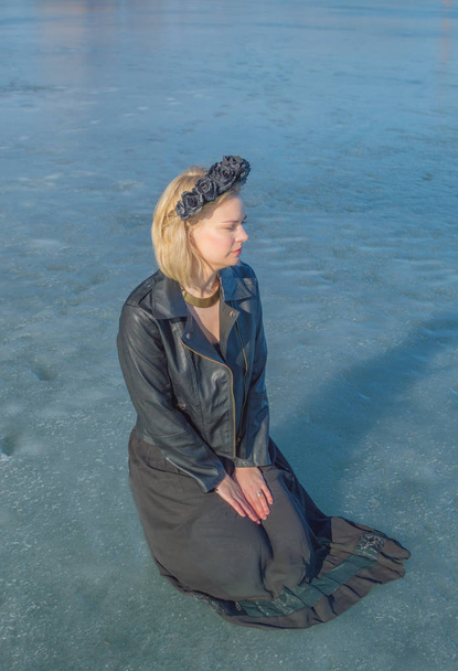 a girl in a black wreath sits on the ice. - Фото, зображення